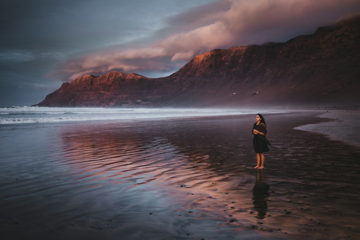 A person on a quiet beach with cliffs in the distance