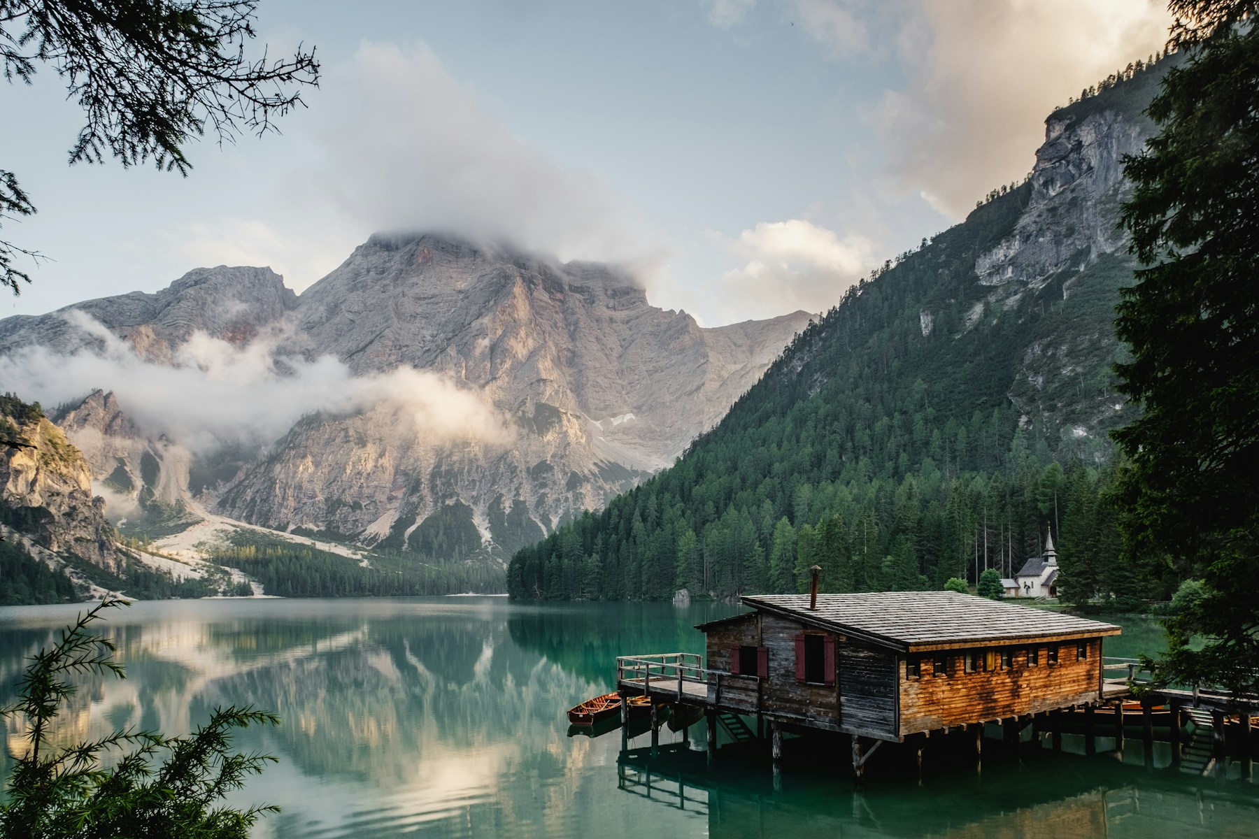 A still alpine lake reflecting mountains and a small cabin at dusk